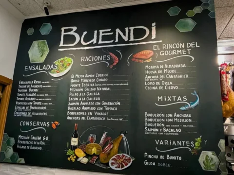 Pizarra verde con el nombre Buendi y dibujos de una botella, una copa y aceitunas